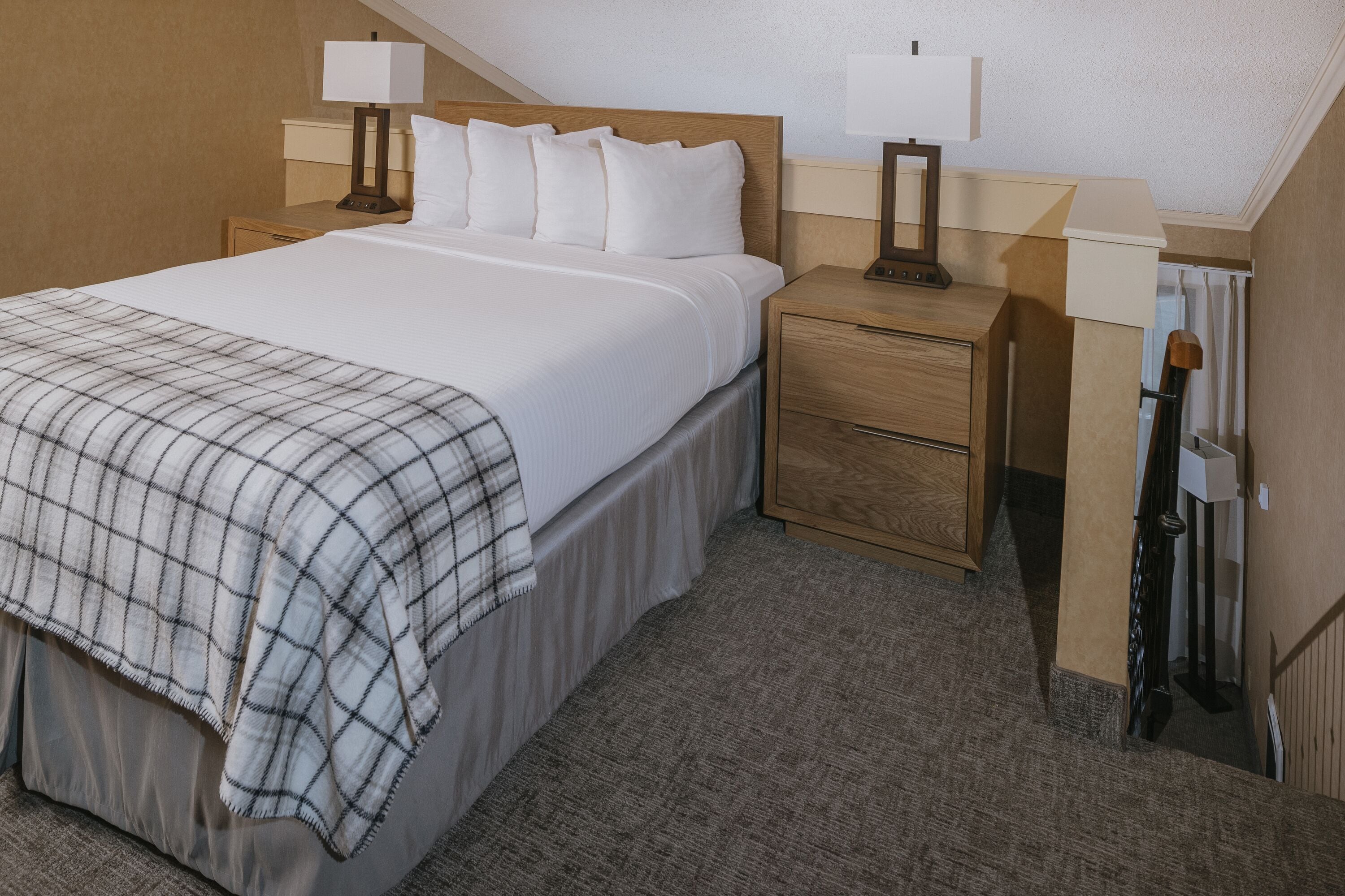 Una cama bien hecha con una manta escocesa, dos mesitas de noche con lámparas y un cabecero de madera.