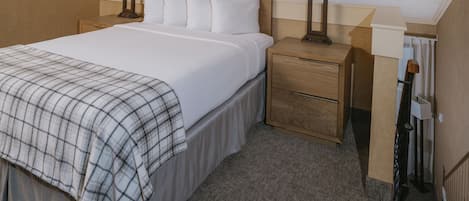 Una cama bien hecha con una manta escocesa, dos mesitas de noche con lámparas y un cabecero de madera.