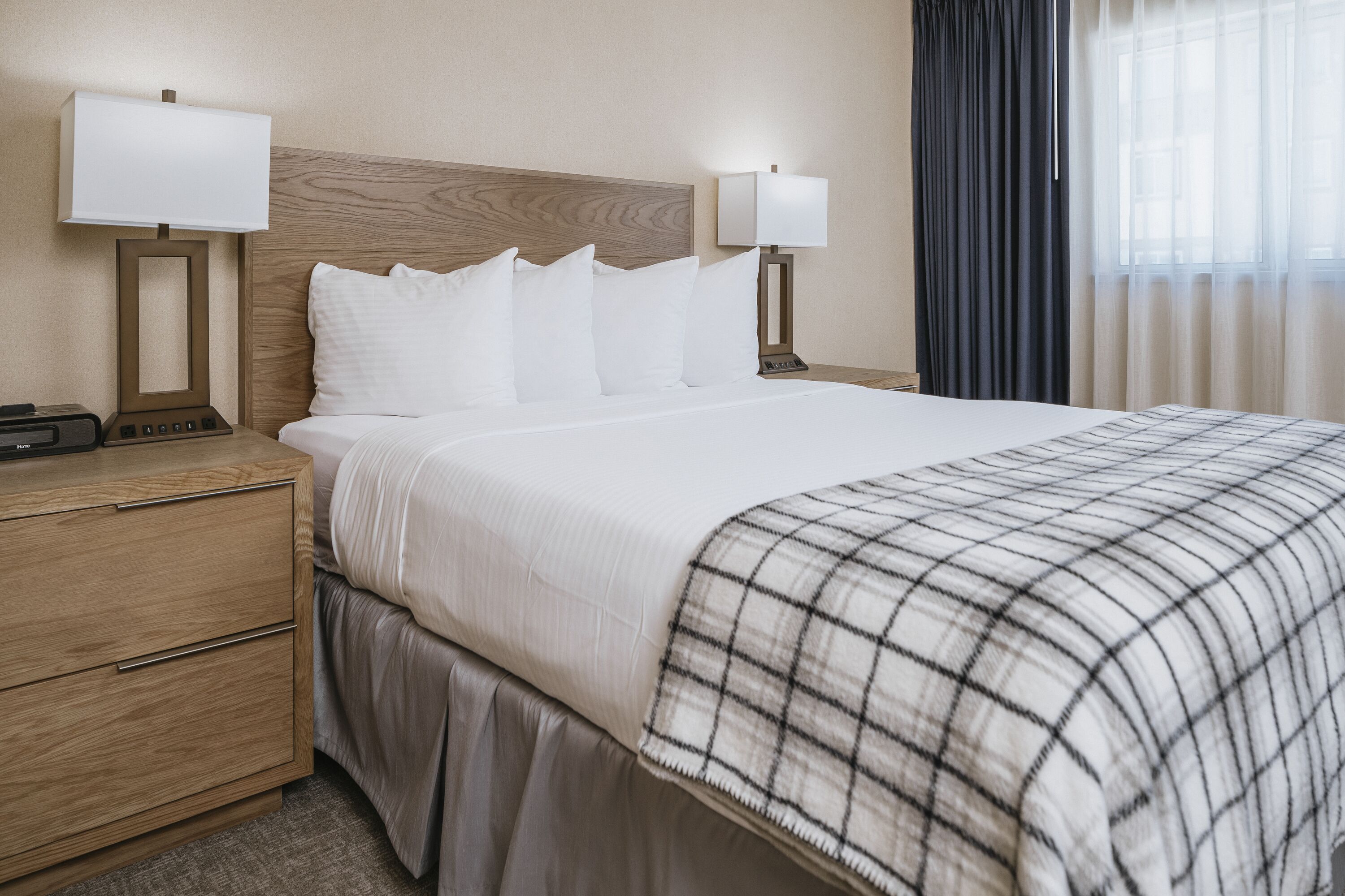 A hotel room with a large bed, two bedside tables with lamps, a wooden headboard, and a window with curtains.