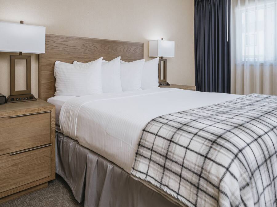 Hotellihuone, jossa on suuri sänky, kaksi yöpöytää valaisimineen, puinen sängynpääty ja ikkuna, jossa on verhot.