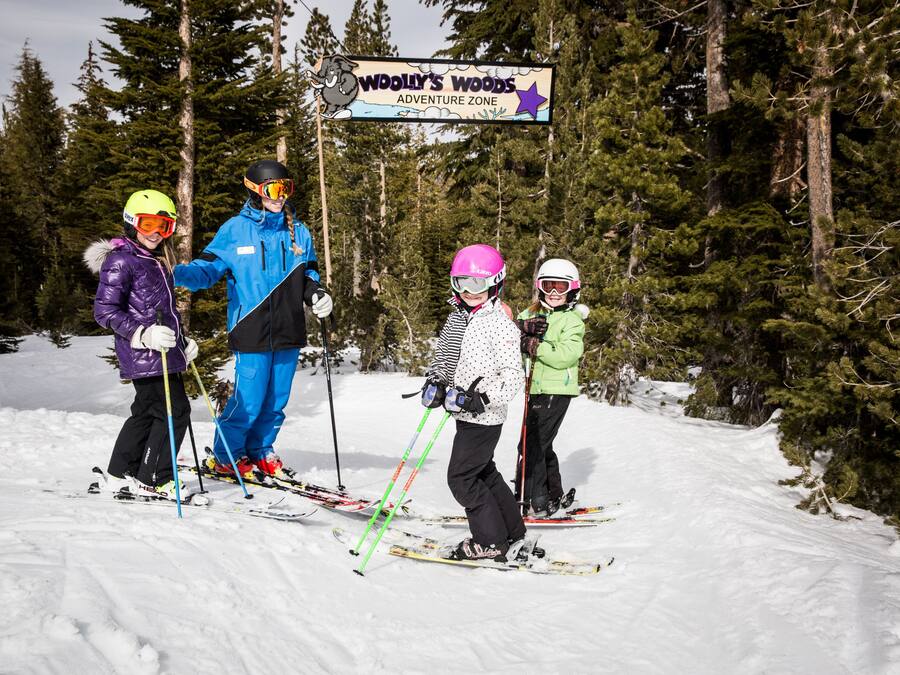 A group of people on skis at a ski resort with a sign reading "Woolly's Woods Adventure Zone".