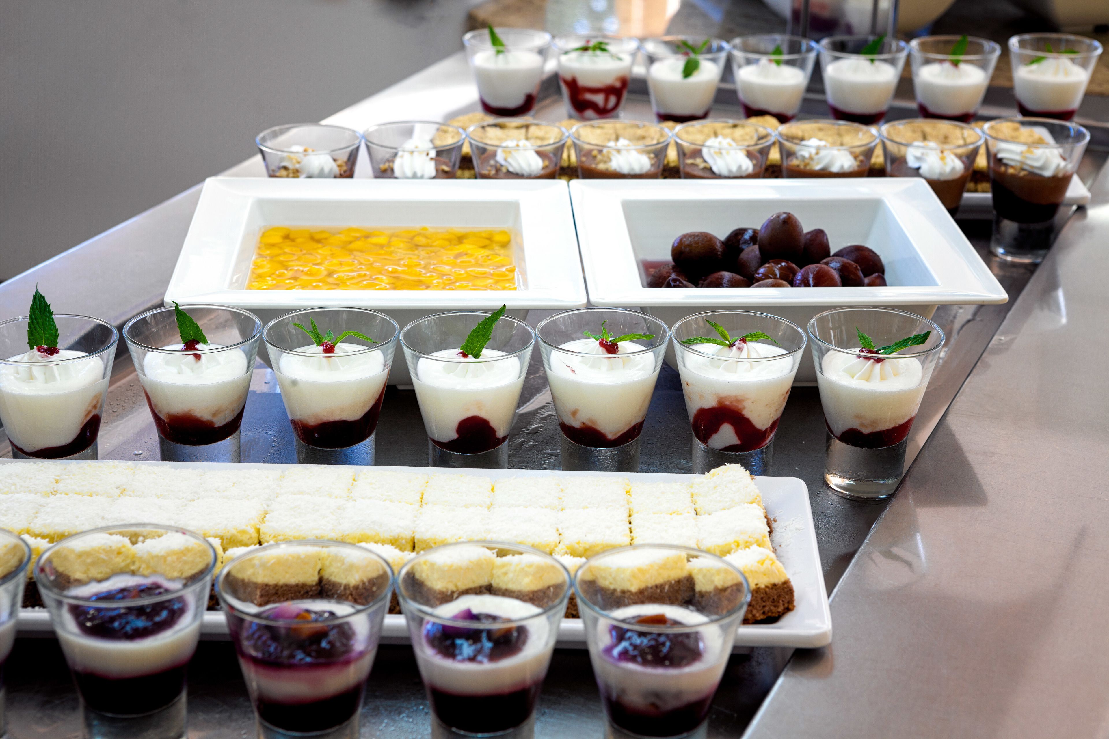 A buffet with various desserts including fruit tarts, layered desserts, and a large rectangular dish of custard.