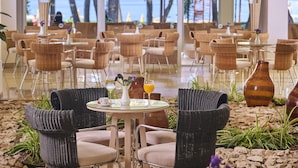 A beachfront restaurant with wicker chairs and tables, a view of the sea, and a tropical garden setting. - Hotel Aurora Plava Laguna (Umag)