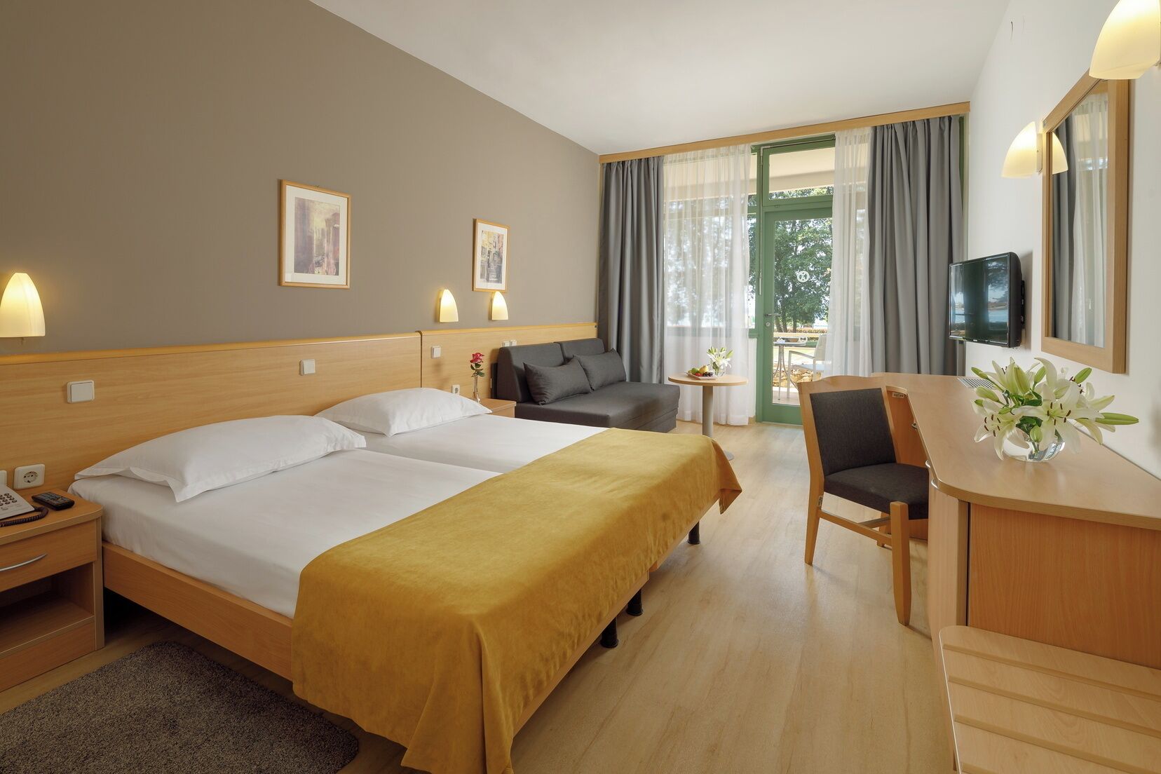 A hotel room with two beds, a sofa, a desk, and a TV.