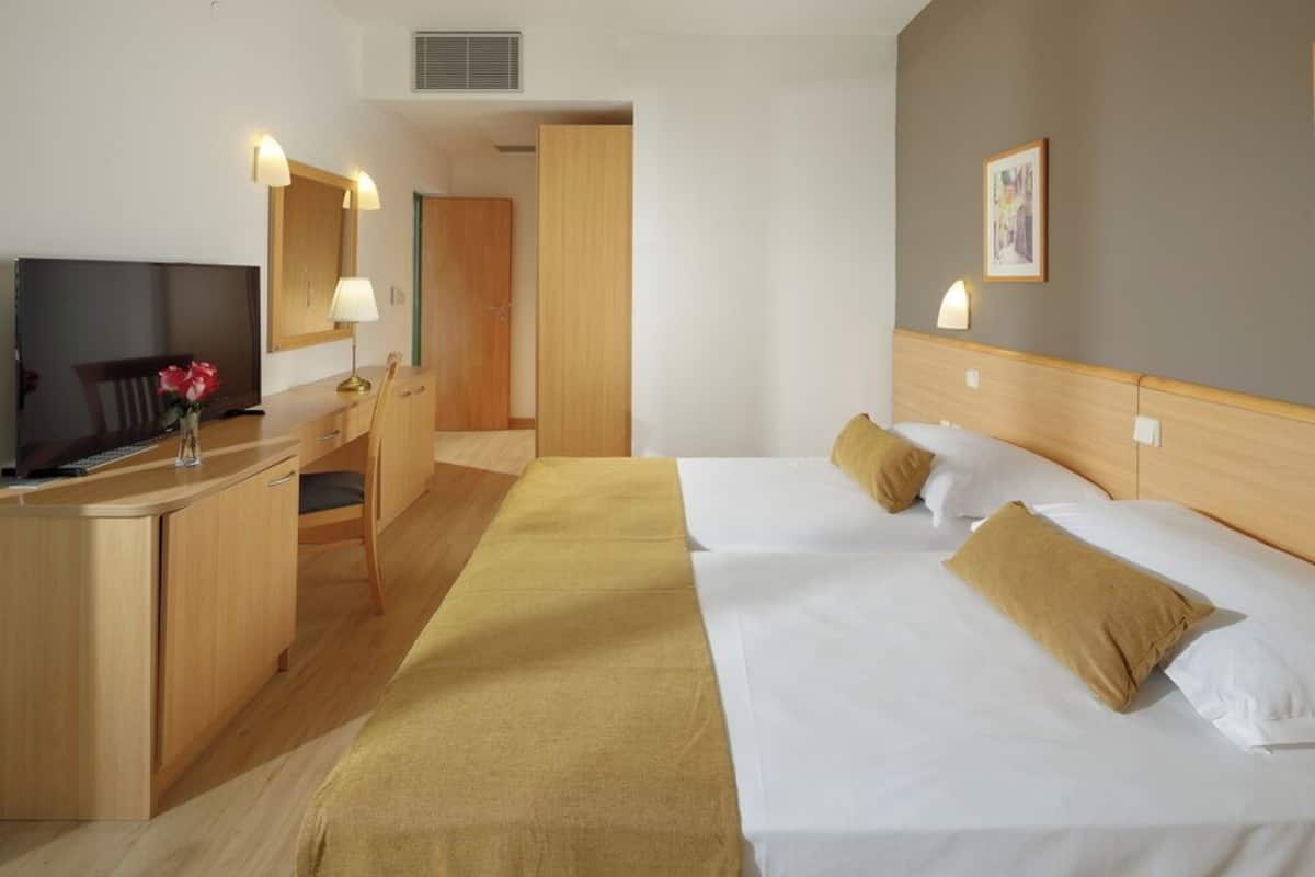 A hotel room with a bed, bedside tables, a desk with a chair, a television, and a mirror.
