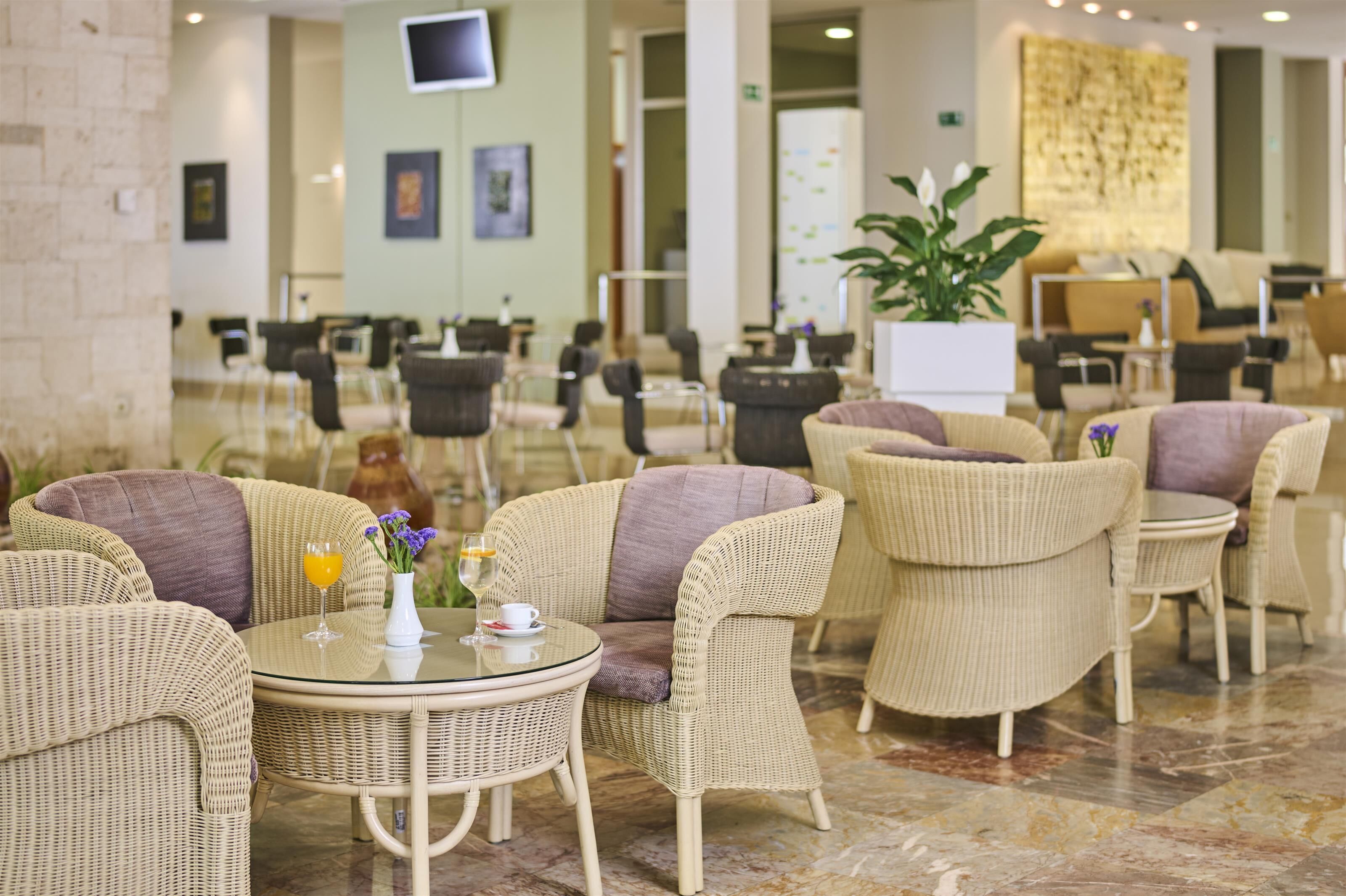 A spacious indoor seating area with wicker furniture and a glass table, featuring a potted plant and a vase with flowers.
