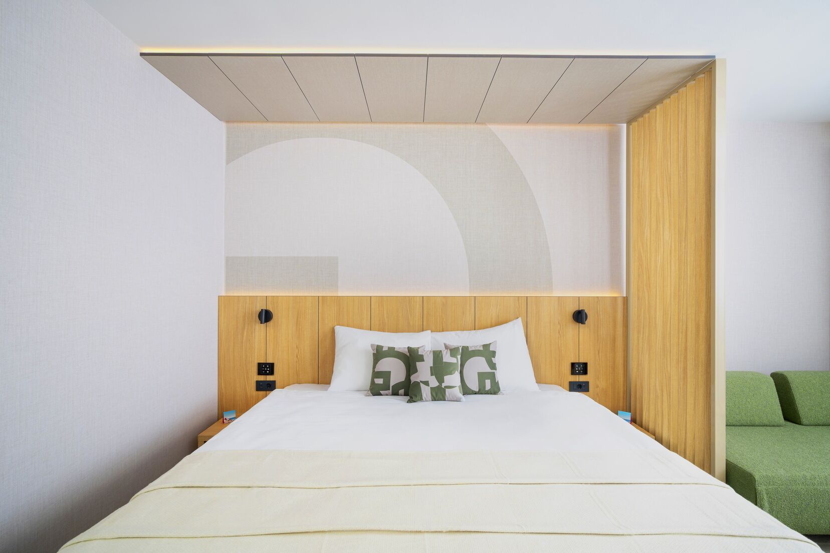 A hotel room with a bed, a wooden headboard, two bedside tables, and a green couch.