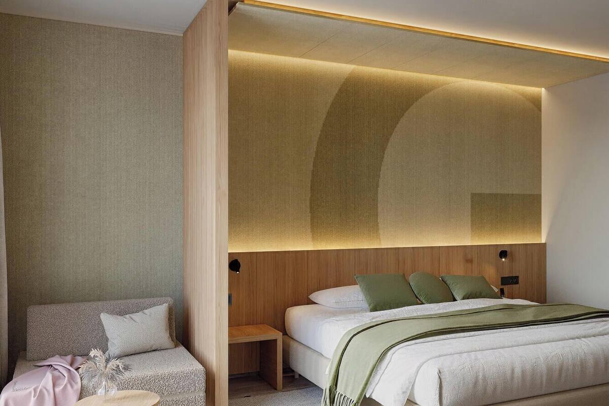 Een moderne hotelkamer met een bed, een zithoek en een houten hoofdeinde met ingebouwde verlichting.