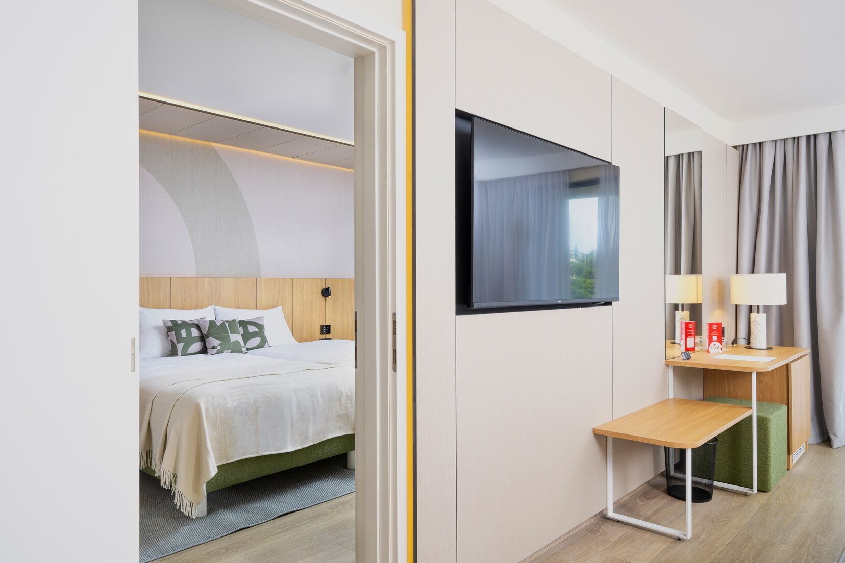A hotel room with a bed, a desk, a flat-screen TV, and a mirror.