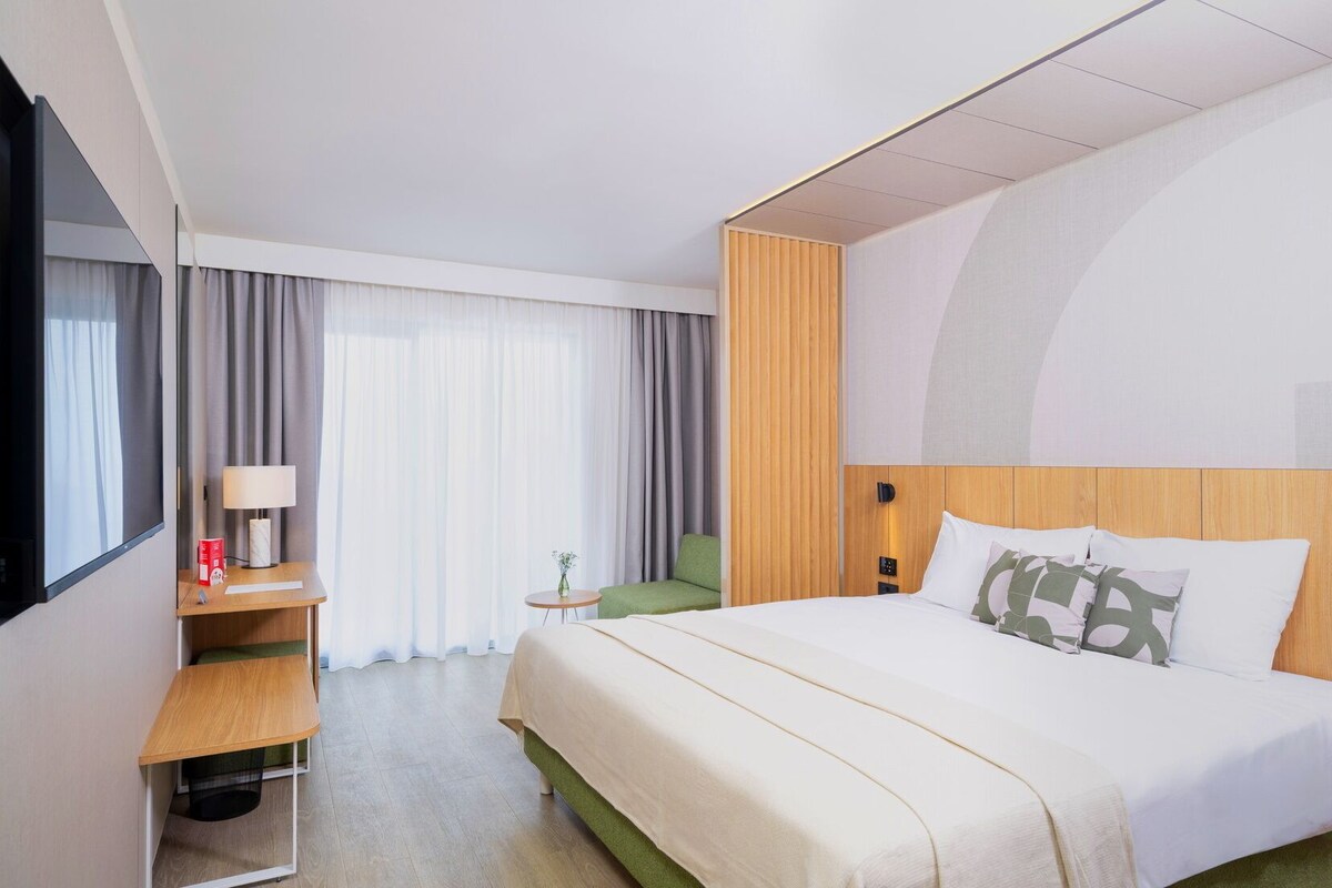 Une chambre d’hôtel avec un lit, un bureau, une chaise et une fenêtre avec des rideaux.