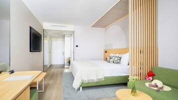 A hotel room with a bed, a desk, a TV, and a green sofa.