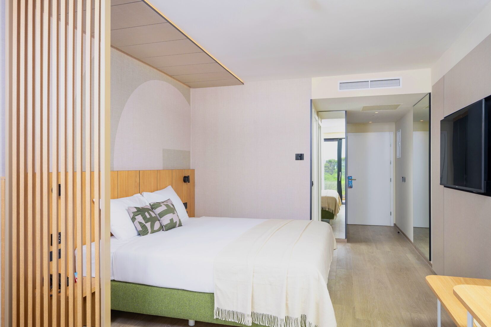 A hotel room with a bed, a TV, and a wooden partition.