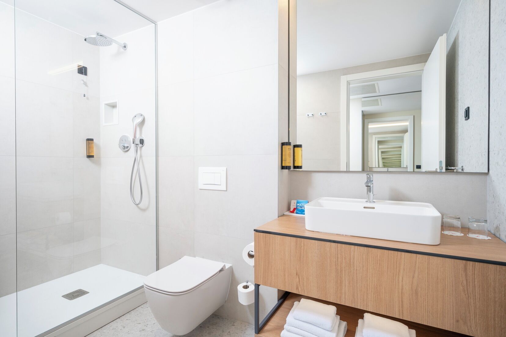 Un baño moderno con ducha de vidrio, inodoro, lavamanos con espejo y toallero.