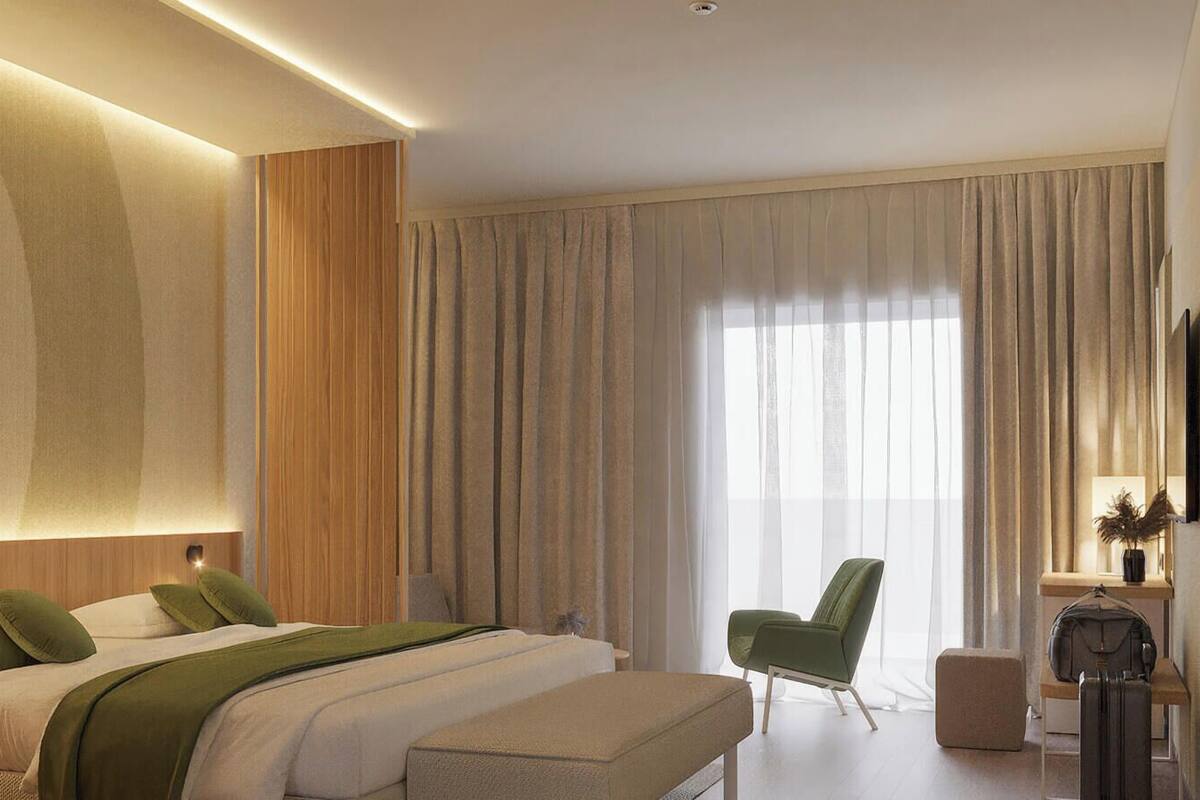 Een moderne hotelkamer met een groot bed, een groene fauteuil, een bureau met stoel en een groot raam met gordijnen.
