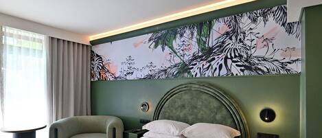 Una habitación de hotel con una cama grande, un cabecero curvo, un mural en la pared, una mesa redonda y una mesita de noche.