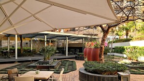 An outdoor patio area with tables and chairs, surrounded by planters and a large tree. - City Lodge Hotel Umhlanga Ridge (Umhlanga)