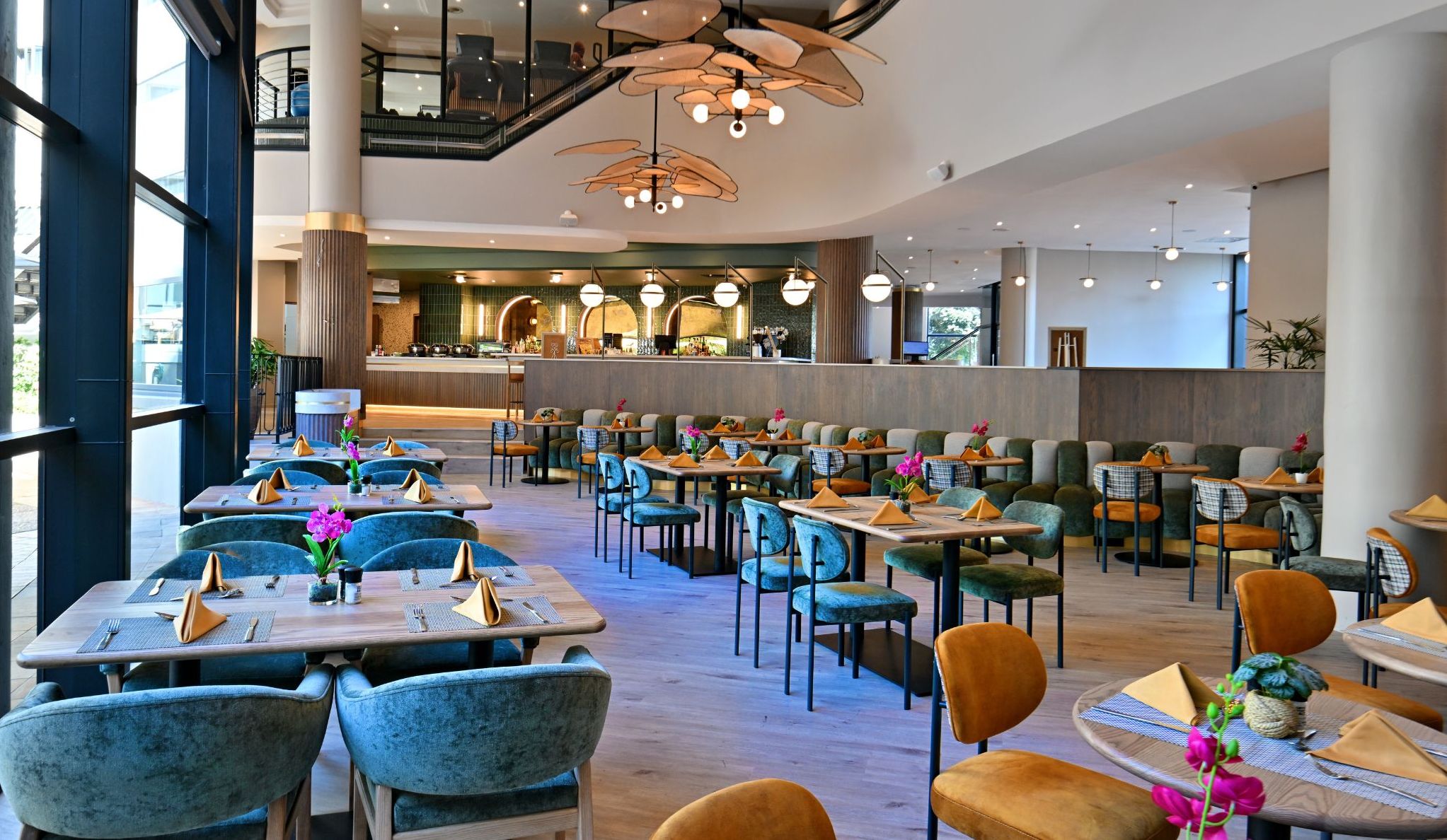A spacious, modern dining area with multiple tables and chairs, a central counter, and a staircase leading to an upper level.