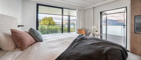 A bedroom with a large bed, a view of mountains, and a balcony with a plant.