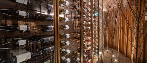 A wine cellar with rows of wine bottles on shelves, a wooden wall, and a tree in the center.