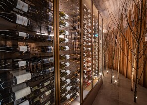A wine cellar with rows of wine bottles on shelves, a wooden wall, and a tree in the center.
