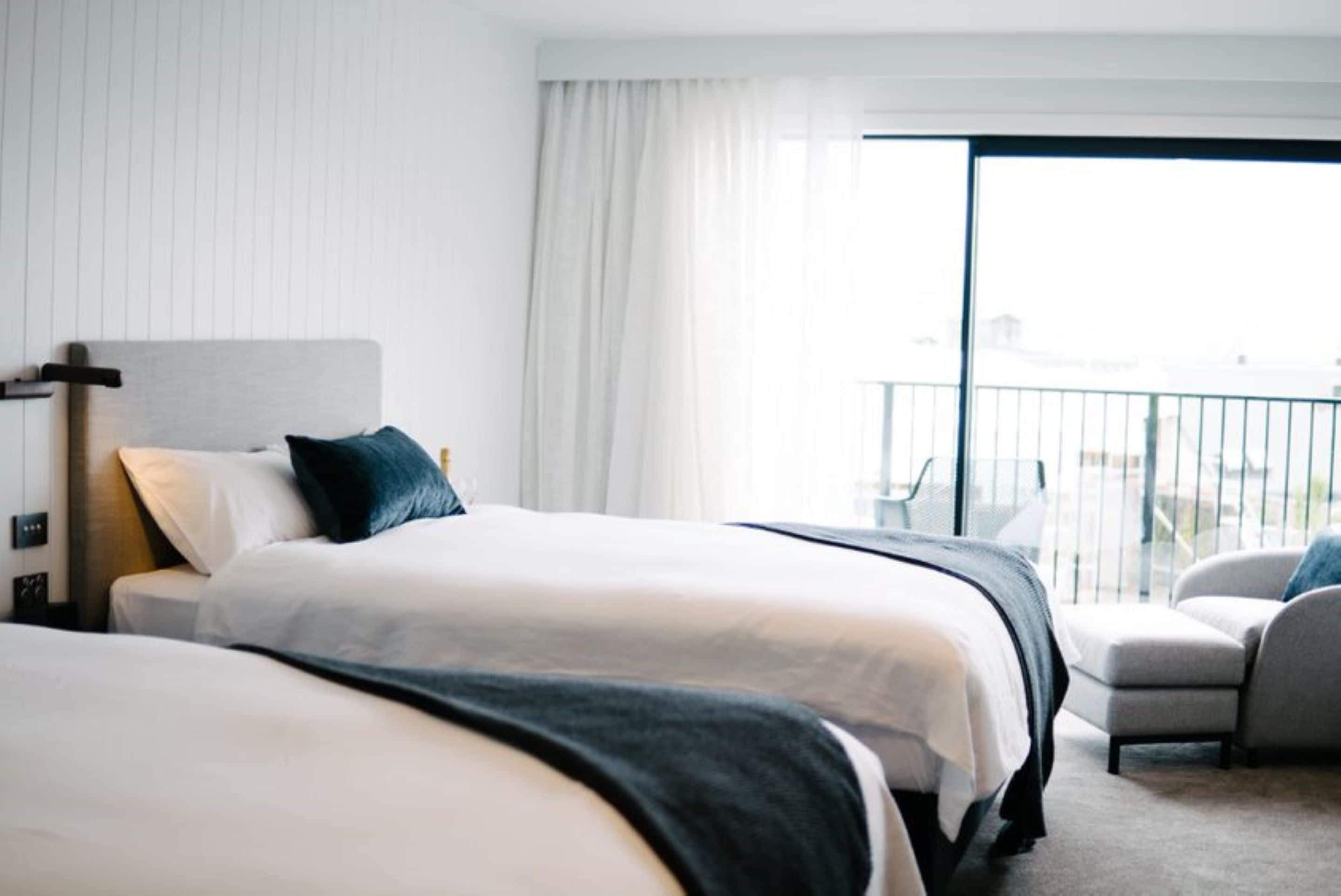 Une chambre d’hôtel avec deux lits, un balcon doté d’une rambarde et une vue sur le paysage urbain.