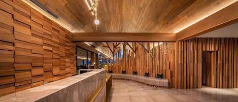Un interior moderno con paneles de madera, un mostrador de recepción de mármol y una zona de estar con un banco curvo.
