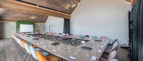 Une salle de conférence moderne, dotée d’une longue table, de chaises colorées et d’un plafond en bois.