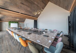 A modern conference room with a long table, colorful chairs, and a wooden ceiling.