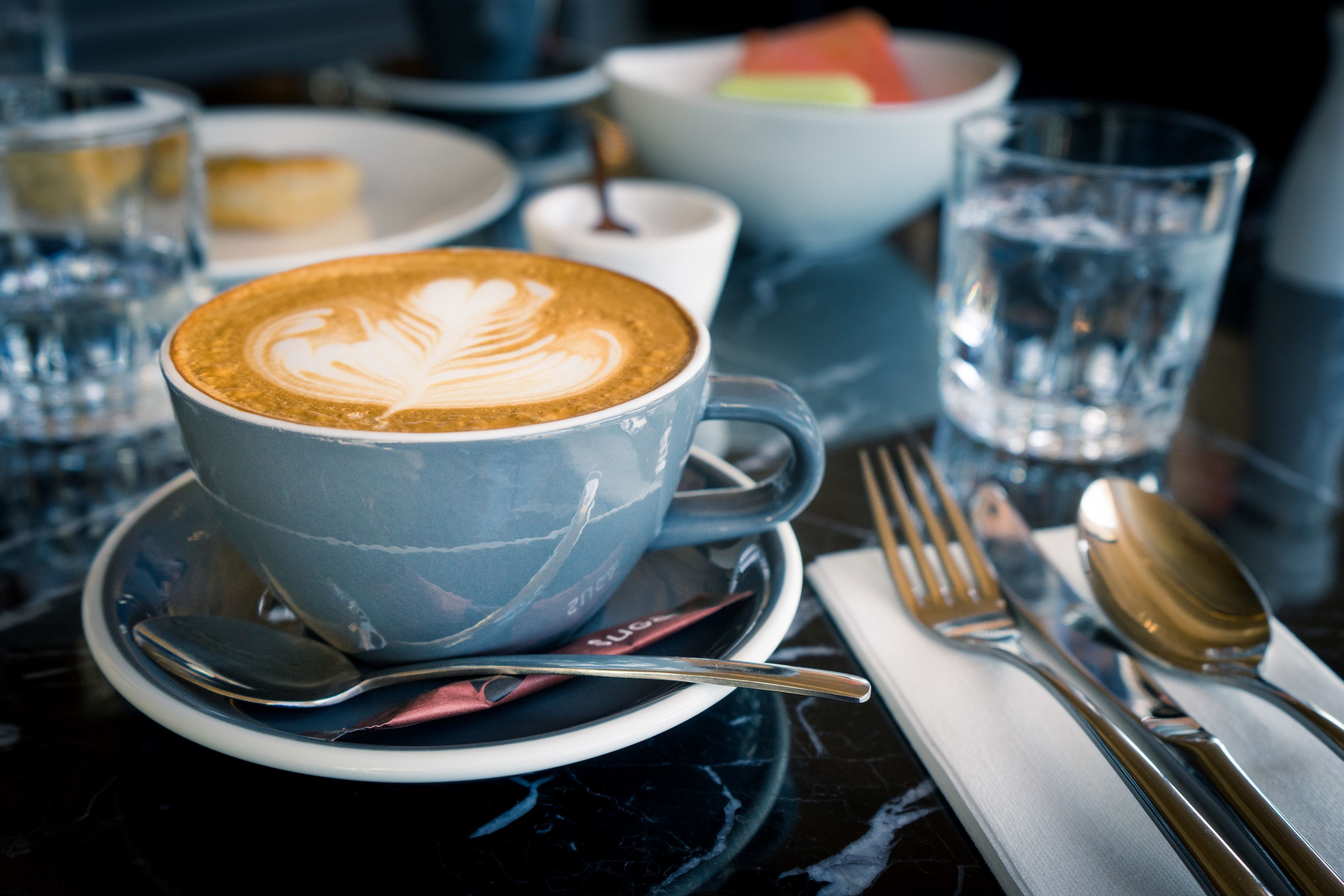 Une table avec une tasse de café bleue, un verre d’eau et un bol de fruits.