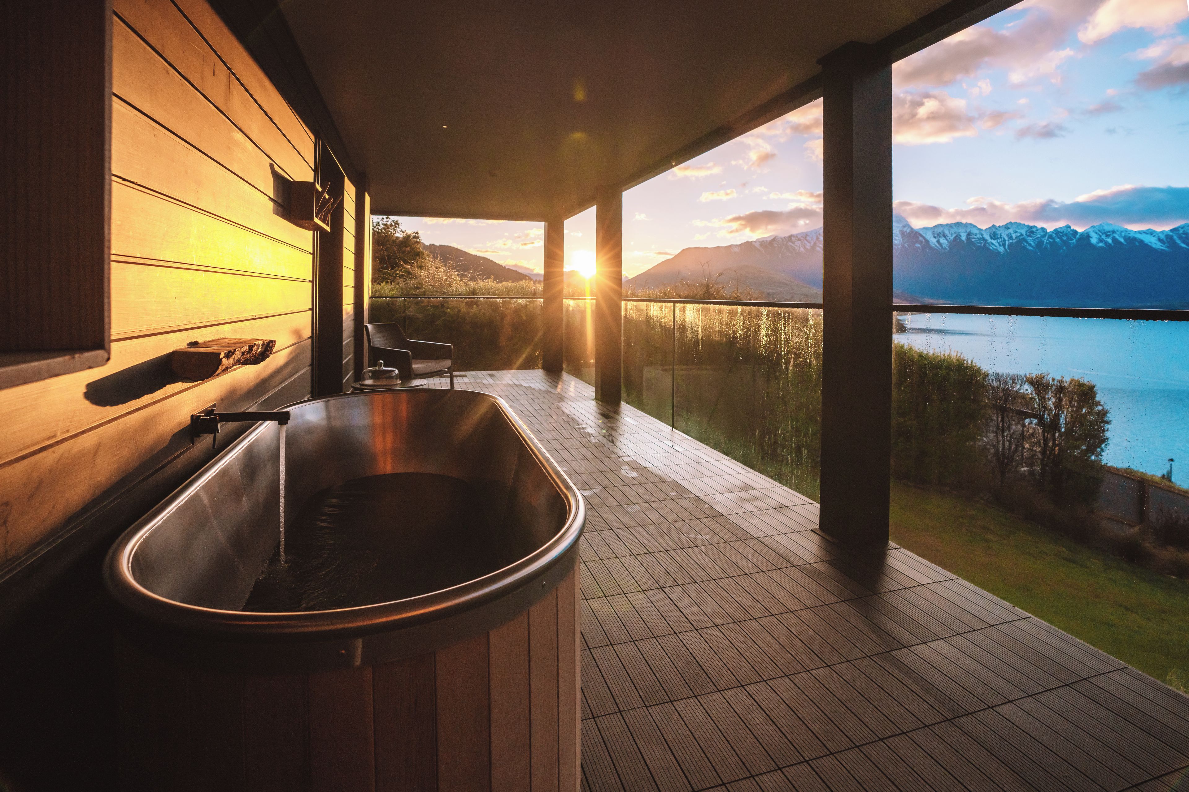 A modern bathroom with a large bathtub, wooden paneling, and a view of a lake and mountains.