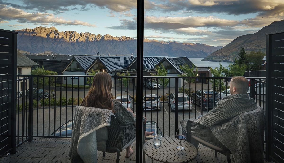 A balcony with two chairs and a table, overlooking a mountainous landscape and a body of water.