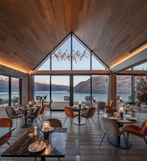 A modern dining area with a high ceiling, large windows, and a view of mountains and a lake. - Kamana Lakehouse (Queenstown)