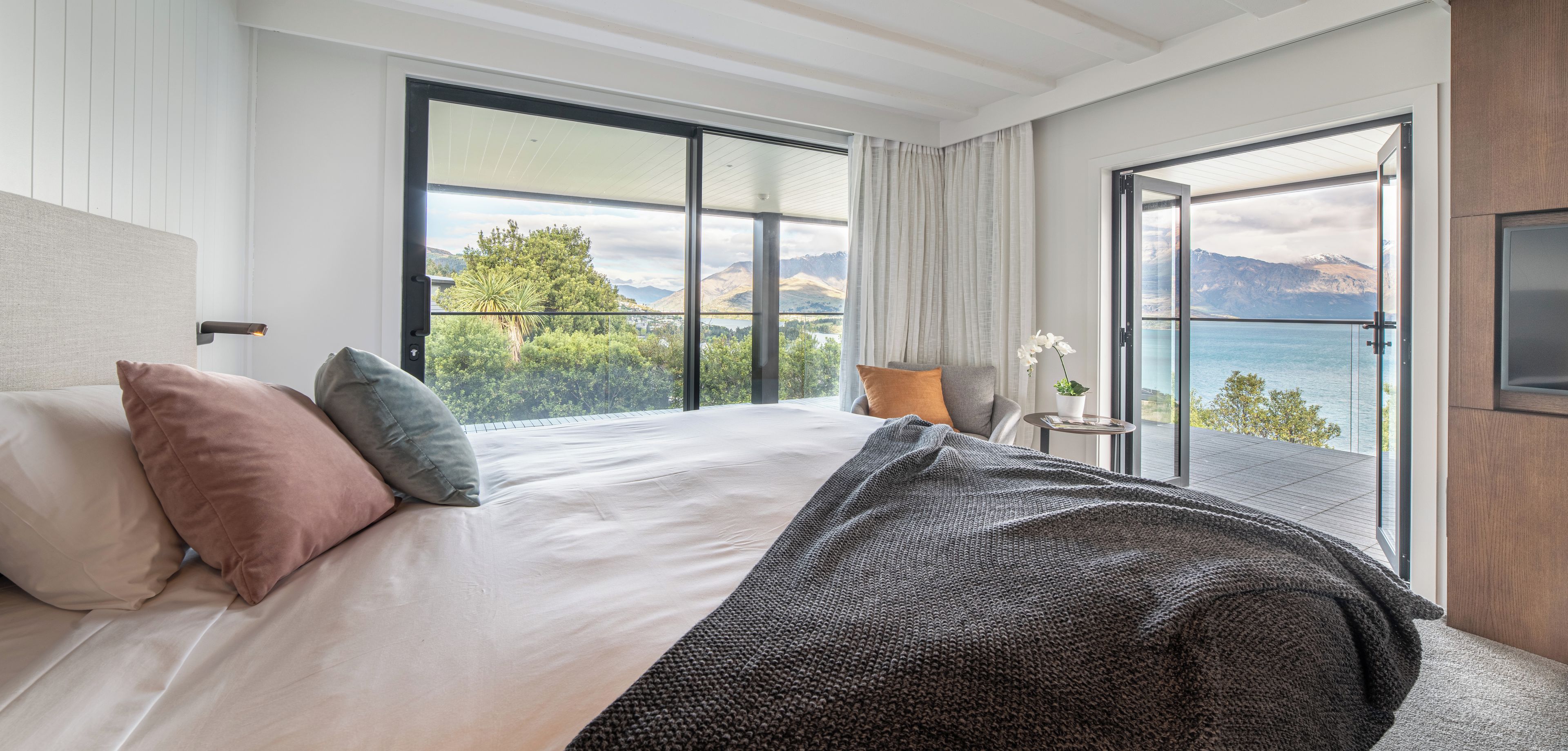 A hotel room with a large bed, a view of the mountains, and a balcony with a view of the sea.