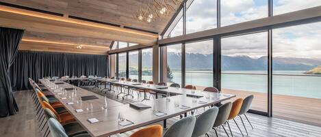 A conference room with a long table, chairs, and a view of mountains and a lake.