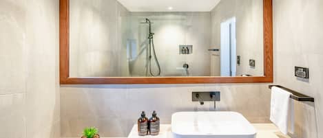 A modern bathroom with a large mirror, a white sink, and a shower.