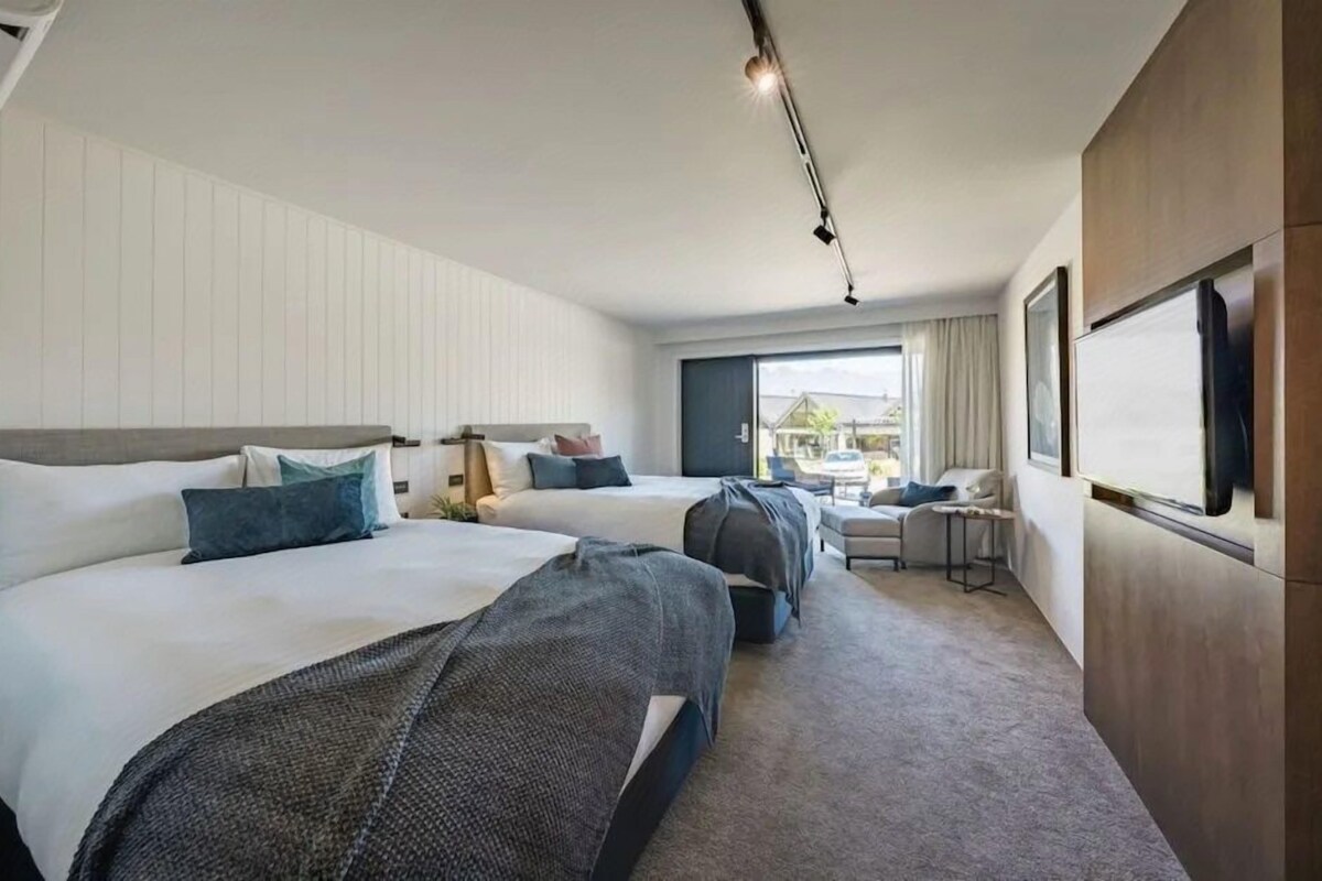 A hotel room with two beds, a desk, a chair, and a large window.