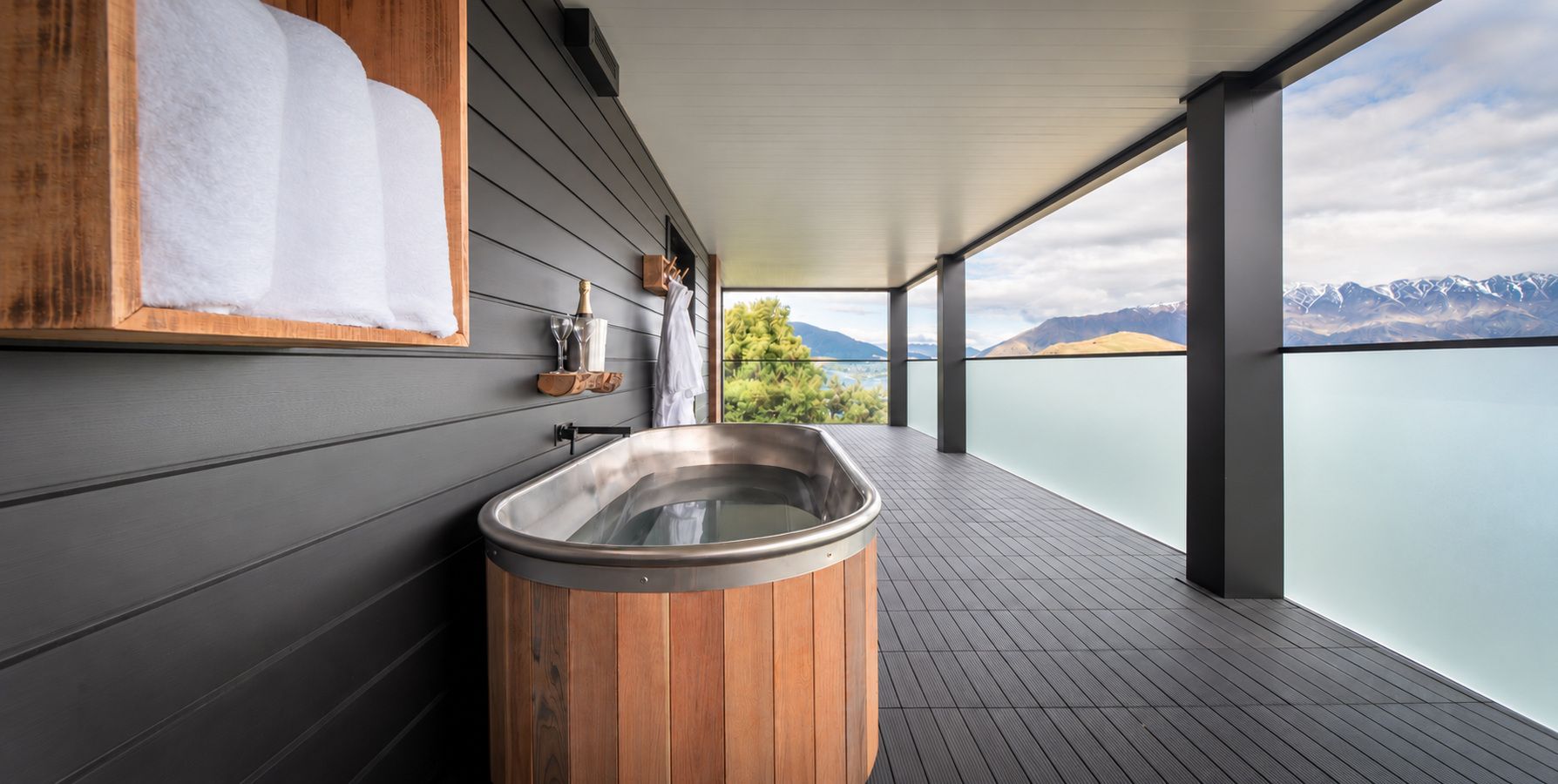 A spa area with a wooden hot tub, a towel rack, and a view of mountains.