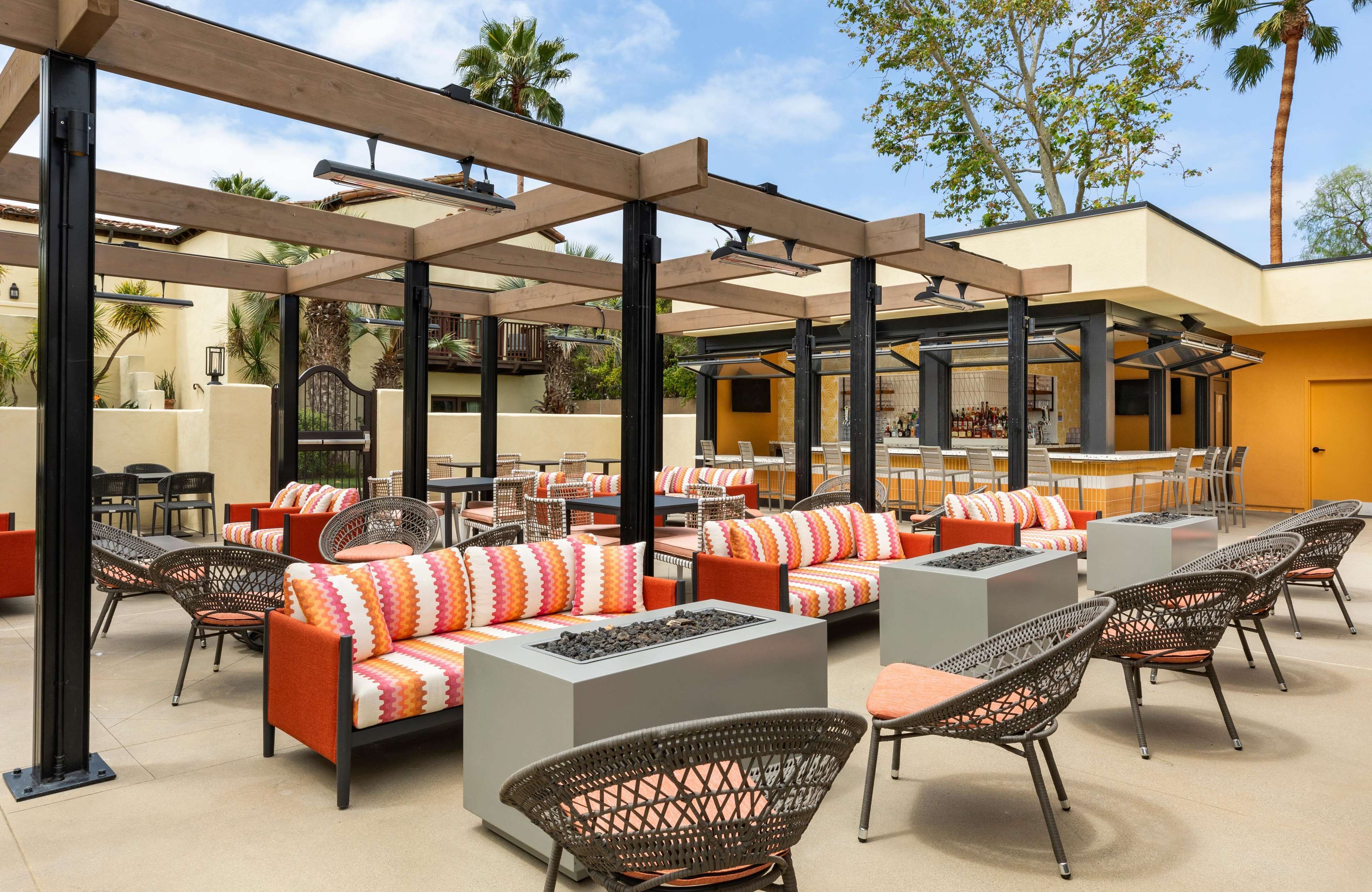 Un patio exterior con varias opciones de asientos, incluyendo sofás y sillas, además de una zona de bar con mostrador.