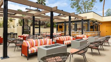 Un espace extérieur aménagé en terrasse, avec différents types de sièges, notamment des canapés et des fauteuils, ainsi qu’un bar doté d’un comptoir.