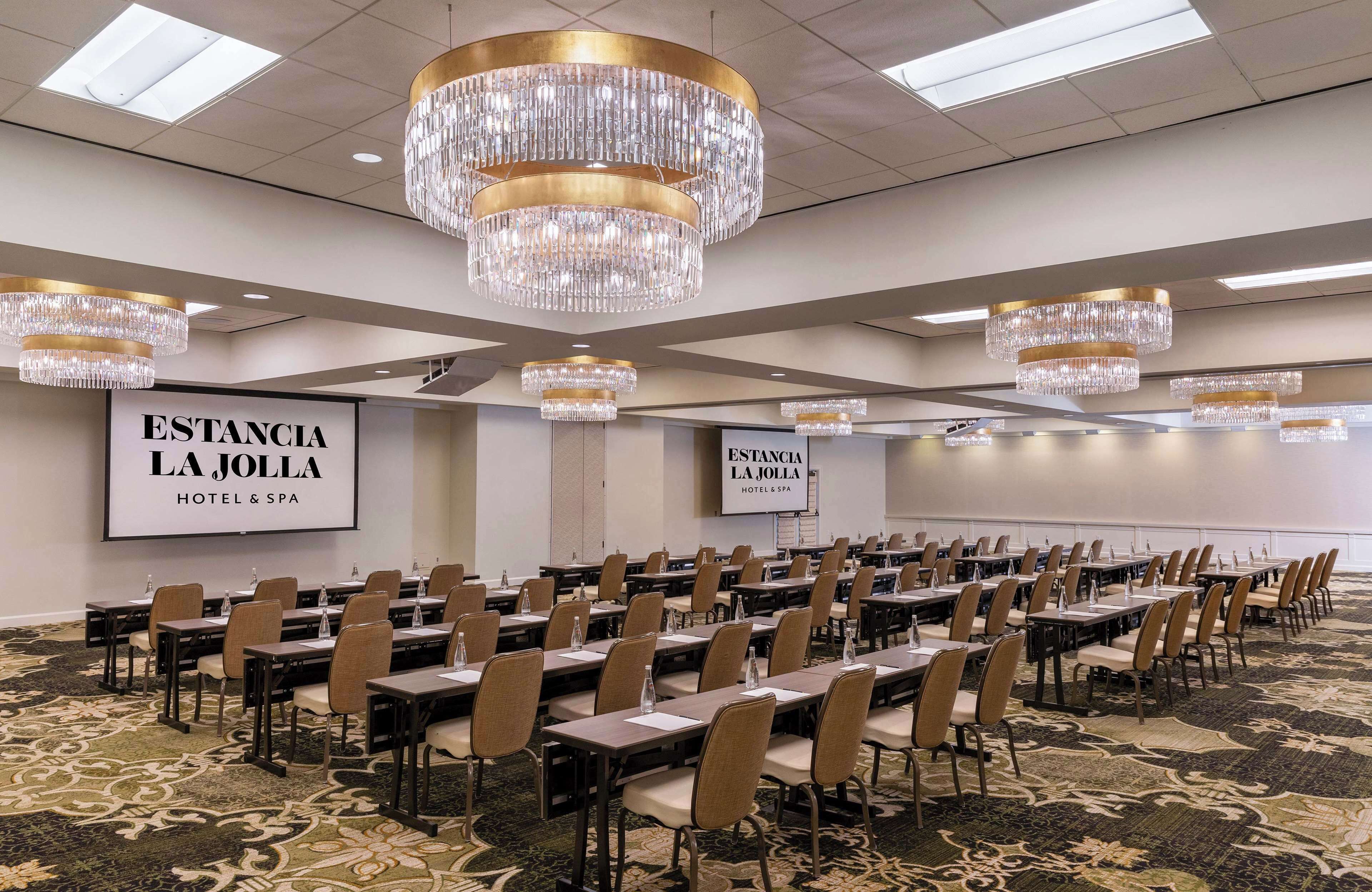 Un salón de conferencias con filas de mesas y sillas, candelabros y señalización para Estancia La Jolla Hotel & Spa.