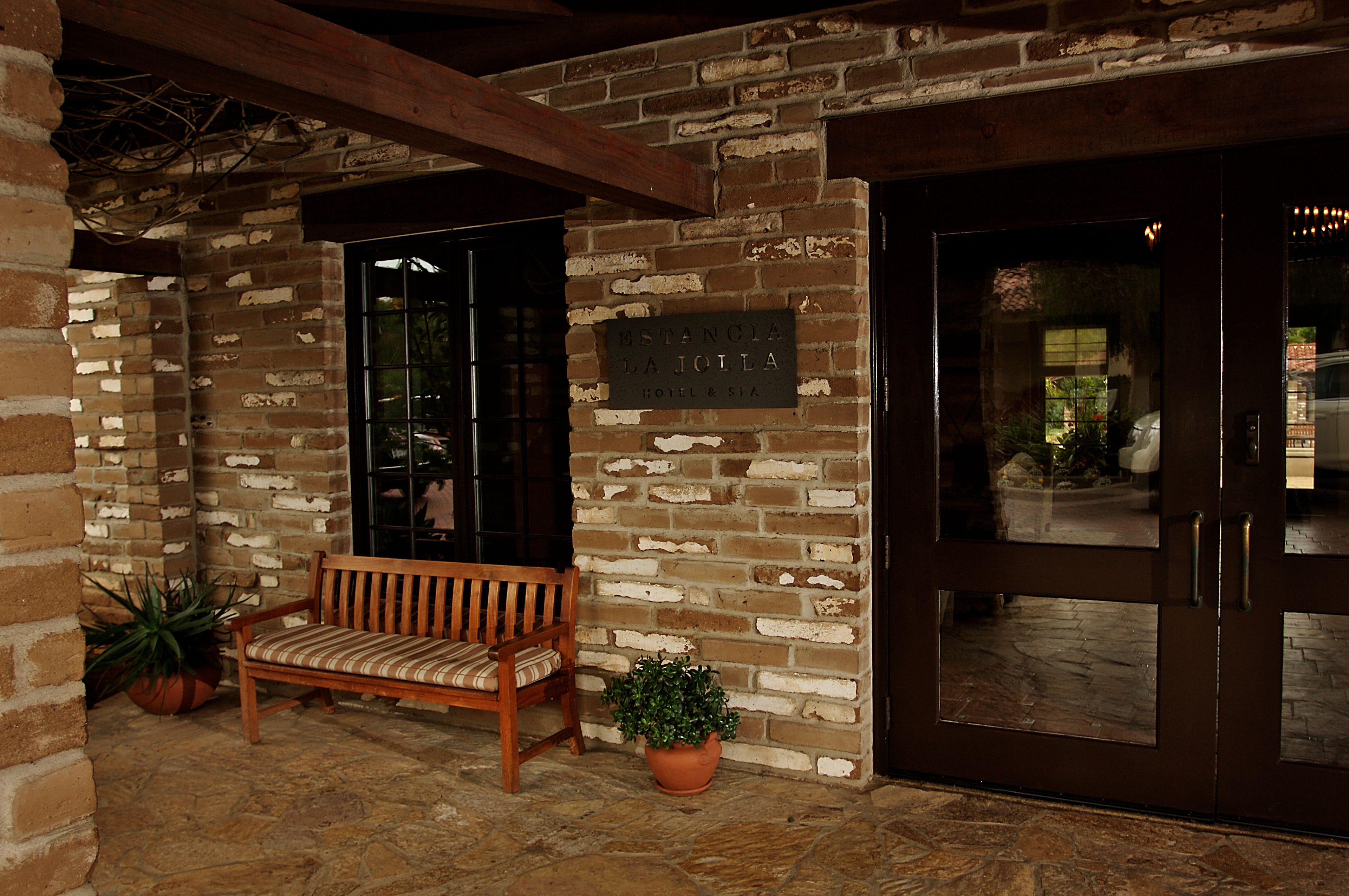 A brick exterior wall with a wooden bench and potted plants.
