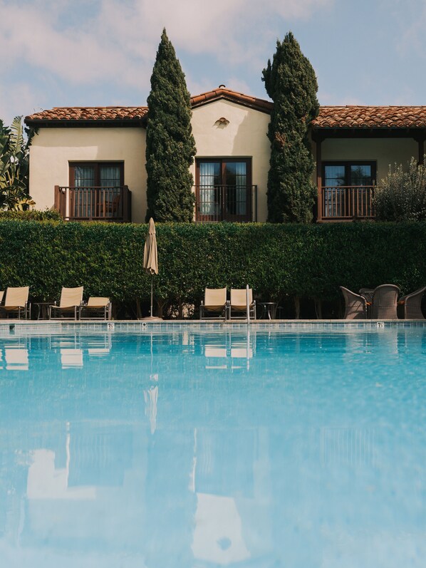 A swimming pool with lounge chairs and a hedge.
