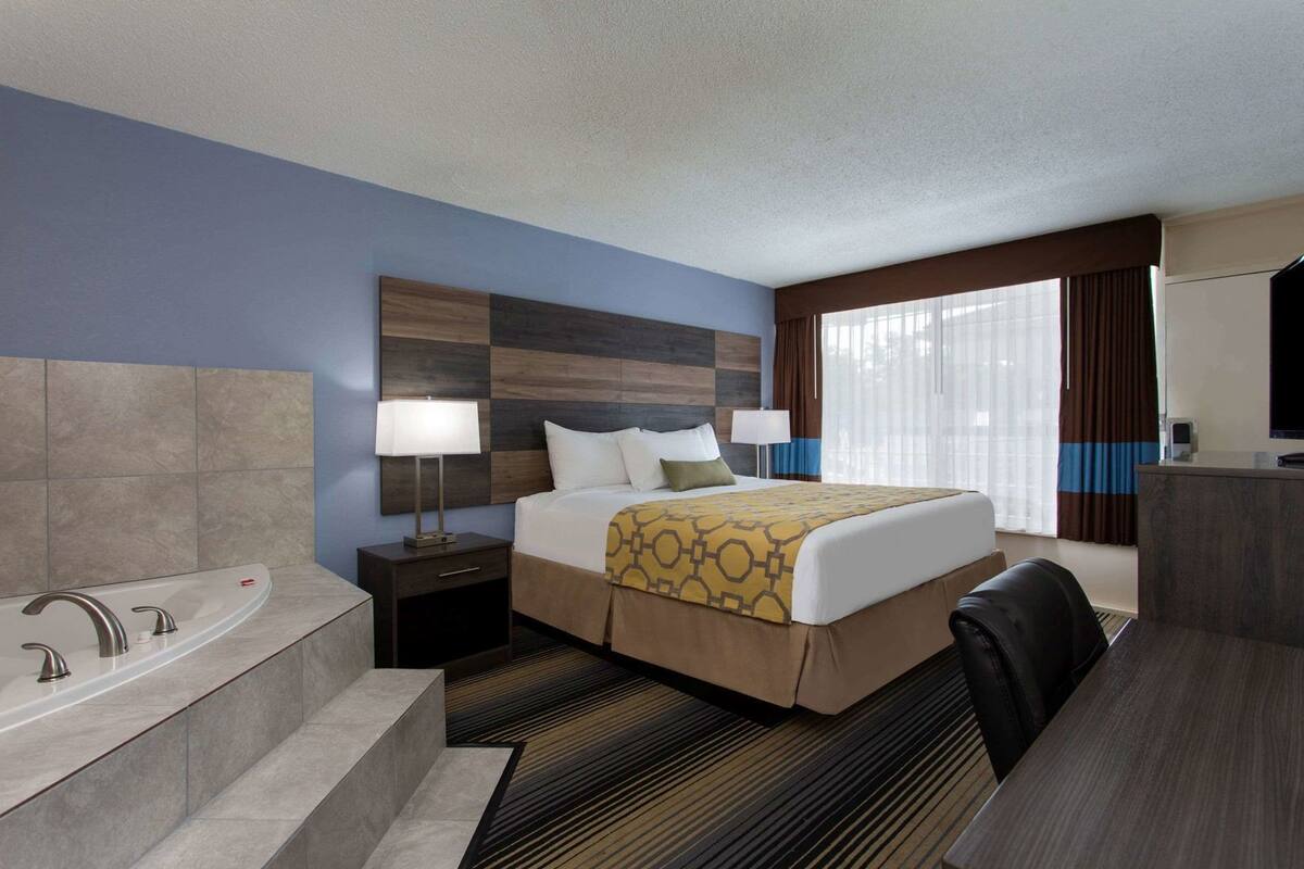 A hotel room with a bed, a desk, a chair, a desk lamp, a TV, a bathroom with a bathtub and sink.