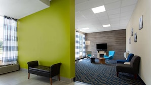 Un vestíbulo de hotel con una pared verde decorativa, una alfombra estampada y asientos modernos, incluyendo un sillón azul y un sofá marrón.