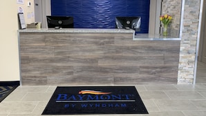 Un mostrador de recepción con una pared azul texturizada, dos monitores de computadora y una alfombra negra con el logotipo de "Baymont by Wyndham".