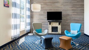 Habitación de hotel con un televisor grande, dos sillones, una chimenea y una alfombra estampada.