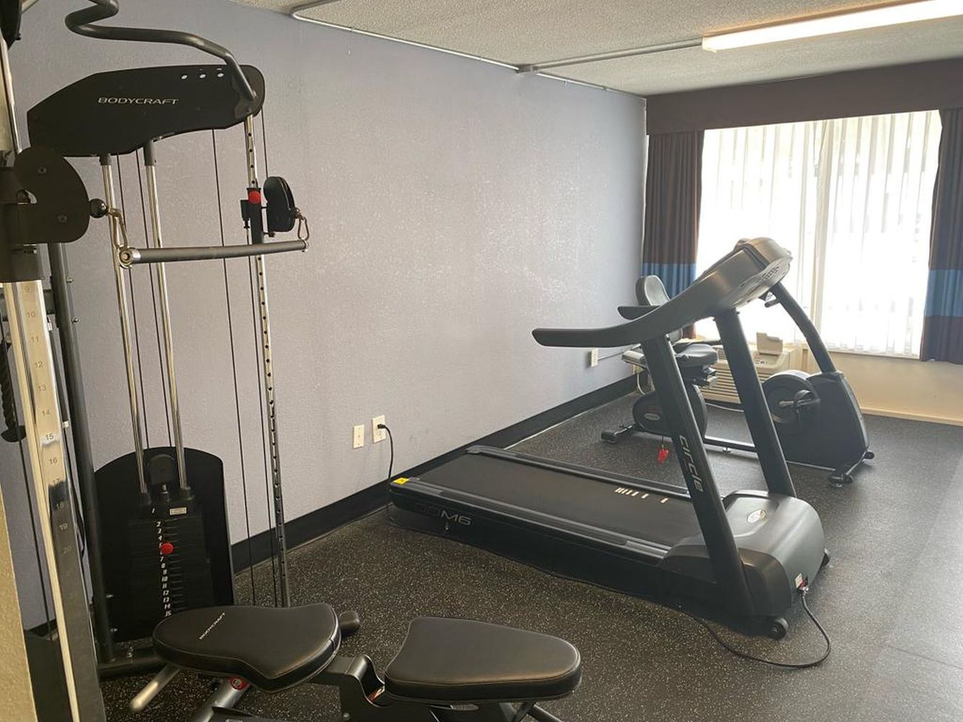 A gym with a treadmill, weight bench, and a bodycraft machine.
