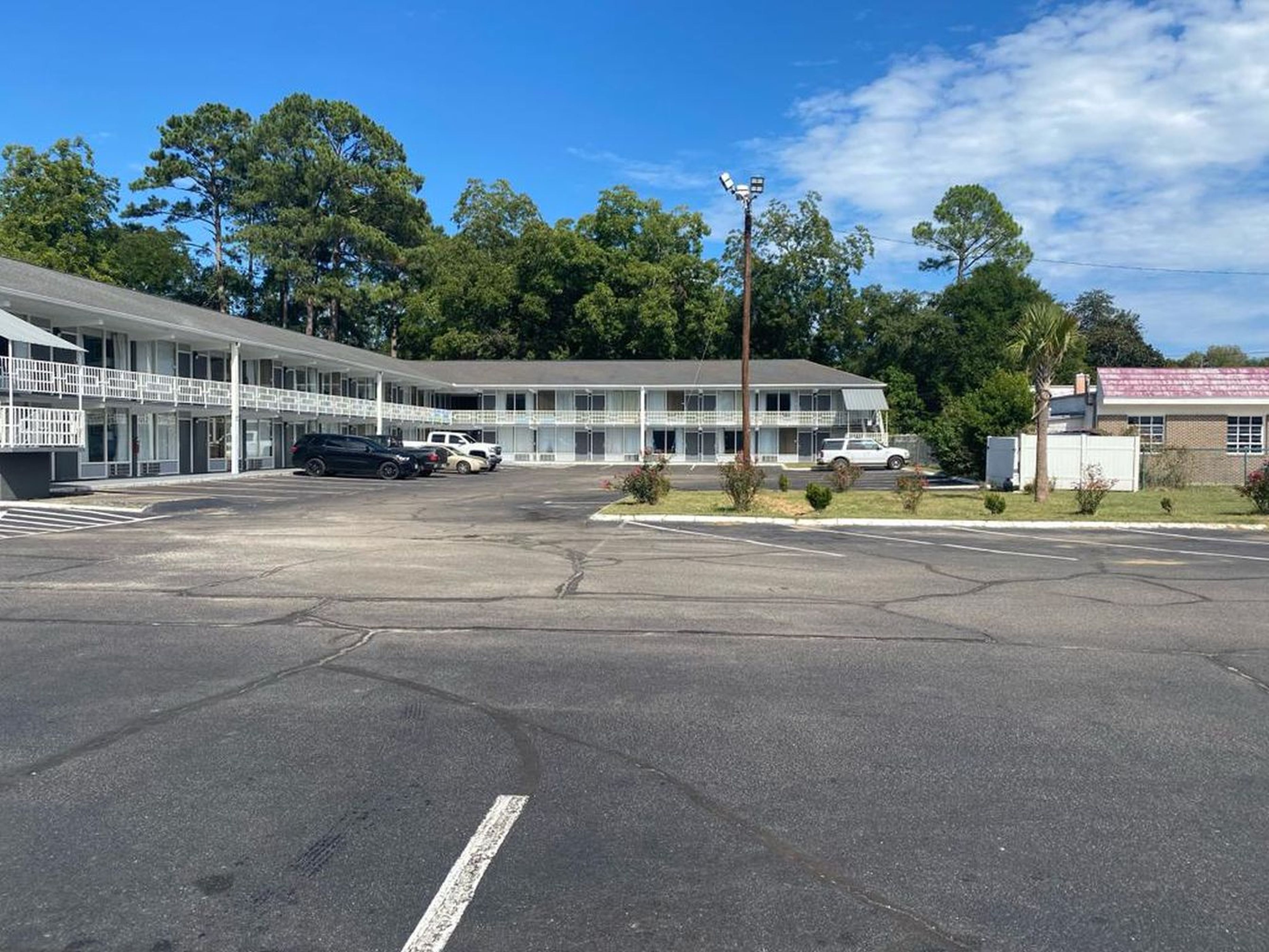 A motel with a large parking lot, a covered walkway, and a building with multiple windows and a flat roof.