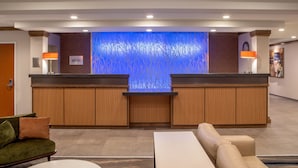 A hotel reception area with a modern design, featuring a reception desk, seating area, and a decorative wall with a blue abstract pattern. - Fairfield Inn & Suites by Marriott Saratoga Malta (Ballston Spa)