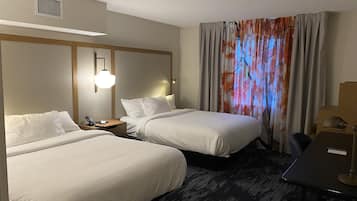 A hotel room with two beds, a desk, a chair, and a large window with curtains.